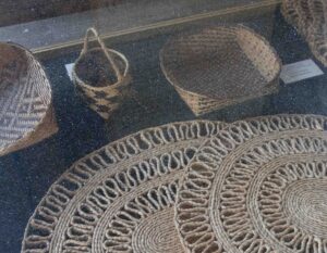 Looking into a display case of woven sweetgrass designs, coated with a thick layer of dust.